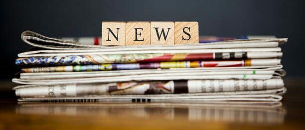 Pile de journaux avec au-dessus des lettres en bois qui écrive le mot "News".